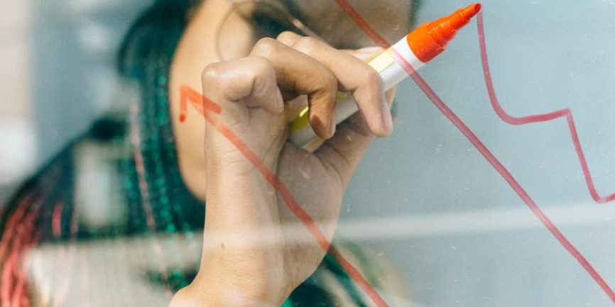 woman in a beige coat writing on a glass panel using a whiteboard marker